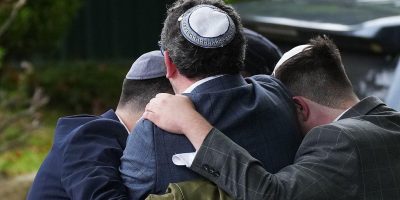 Трое мужчин в еврейских кипах, снятые со спины, обнимаются, обняв друг друга за плечи