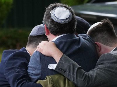 Трое мужчин в еврейских кипах, снятые со спины, обнимаются, обняв друг друга за плечи