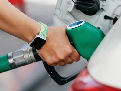 «Чет-нечет». В России придумывают все новые схемы продажи бензина 3 На изображении правая рука человека со смарт-часами на запястье держит зеленый топливный пистолет, который вставлен в бензобак белой машины.