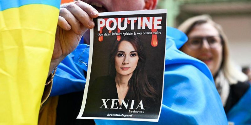 Сторонники Украины устроили акцию протеста на презентации книги Ксении Федоровой в прошлом апреле в Париже - участник акции держит фото Федоровой с надписями "Путин" и "Ксения"