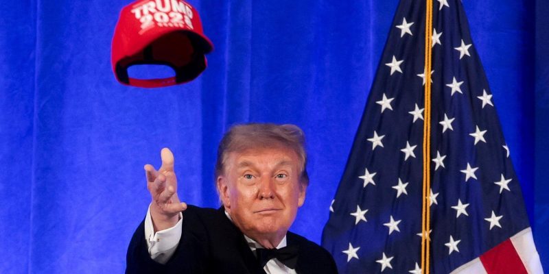 Трамп, кидающий в воздух красную кепку с надписью Trump 2028, за ним — флаг США.