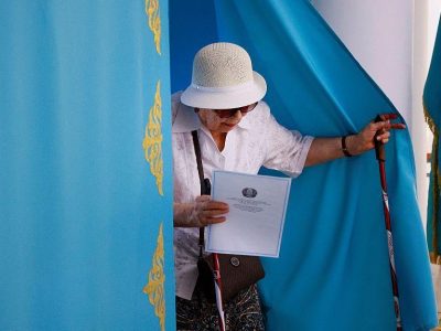 Пожилая женщина выходит из кабинки для голосования с бюллетенем в руках