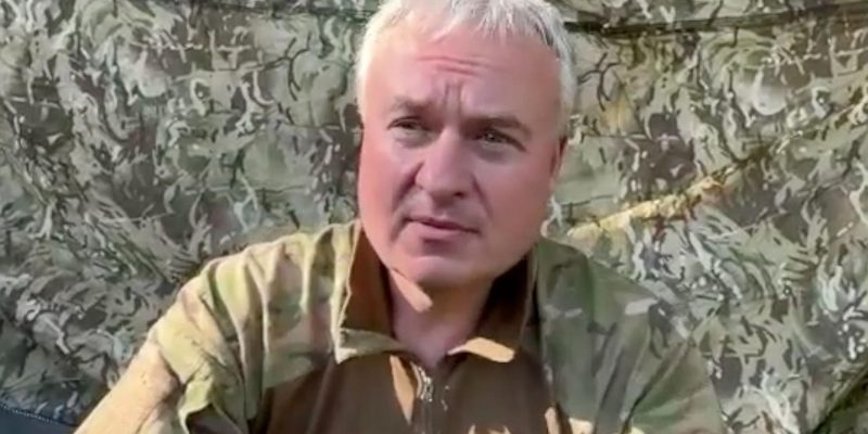 Седой мужчина в камуфляжной форме на фоне маскировочной сетки