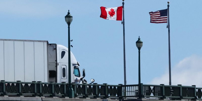 Флаги США и Канады на мосту, по которому проезжает грузовой автомобиль