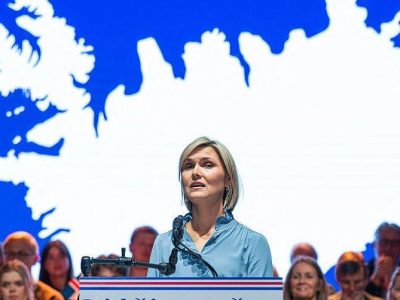 Премьер-министр Исландии Криструн Фростадоуттир выступает с трибуны, за ее спиной большая белая карта Исландии