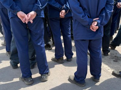 Пленные солдаты украинского происхождения рассказали Би-би-си, почему воевали на стороне России 2 Вид со спины на ряд мужчин в темно-синей военной форме. Они стоят, скрестив руки за спиной.