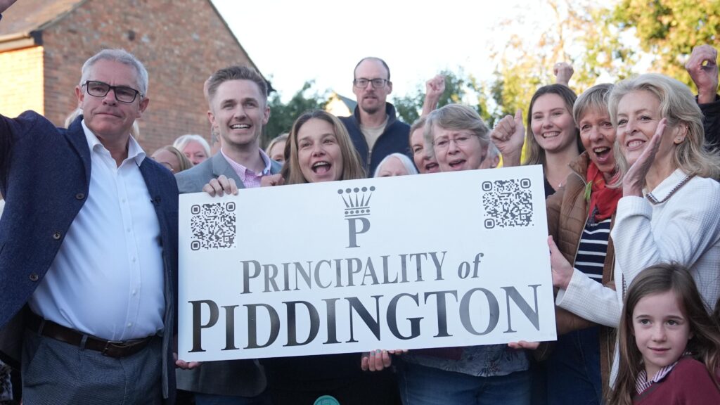 Piddington villagers stand by a sign celebrating after voting overwhelmingly to become an independent state in a symbolic “referendum”