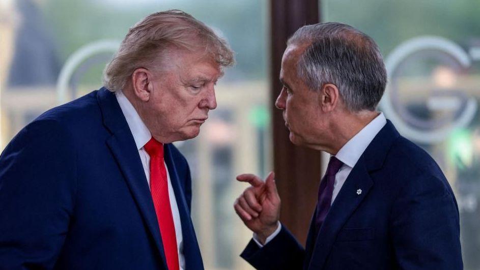 A file image showing U.S. President Donald Trump at a working lunch with Prime Minister Mark Carney and other G7 leaders. The image shows Carney and Trump side by side mid-conversation. Both are wearing a suit. Carney is gesturing with his hand mid-speech, while Trump hangs his head low to listen.