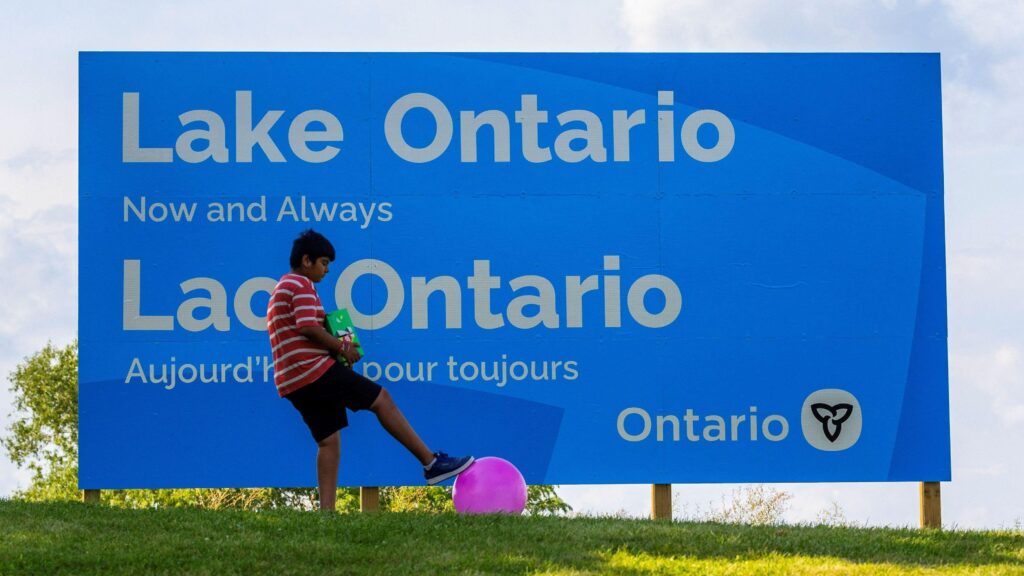 A sign reads "Lake Ontario now and always" with a boy playing with a ball nearby.