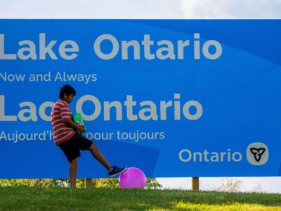 A sign reads "Lake Ontario now and always" with a boy playing with a ball nearby.