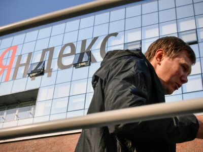 Мужчина со смартфоном перед зданием с вывеской «Яндекс»