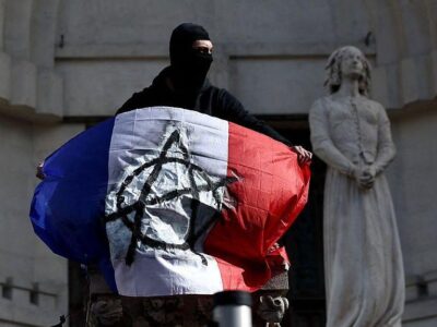 Во Франции возобновились протесты, полиция применяет слезоточивый газ 2 Протестующий в черной маске с флагом Франции, на котором нарисован знак анархии