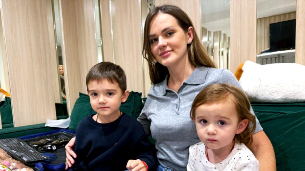 Уехать нельзя остаться. Жители Киева выбирают между добровольной эвакуацией и еще одной зимовкой в городе под обстрелами 1 Женщина с длинными волосами сидит на зеленом диване с двумя маленькими детьми, мальчиком и девочкой