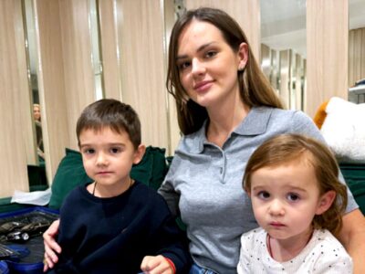 Женщина с длинными волосами сидит на зеленом диване с двумя маленькими детьми, мальчиком и девочкой